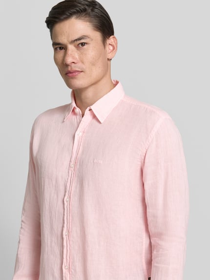 Mannenmodel draagt Regular Fit Freizeithemd aus reinem Leinen Modell 'RELEGANT' van BOSS Orange in effen lichtroze, structuur van puur linnen, kentkraag, doorknoopsluiting, label stitching, lange mouwen met manchetten, detail op de rugpas, voorkant bovenlichaam close-up.