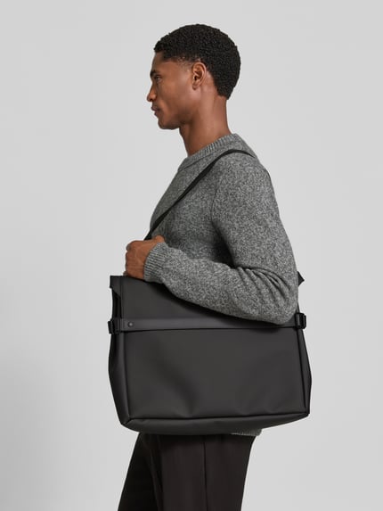 Männermodel trägt Messenger Bag mit Logo-Detail von Rains in Schwarz, glatte Oberfläche, verstellbarer Schulterriemen, Seitenansicht, Nahaufnahme Oberkörper. Hauptfach mit Überschlag, Druckknöpfe, Maße: 48x33x9 cm, Länge Schulterriemen 82 cm.