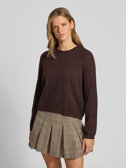 Frauenmodel trägt Regular Fit Pullover mit gerippten Ärmelbündchen Modell 'ADA' von PIECES, braun, texturierte Oberfläche, Ganzkörperansicht von vorne.