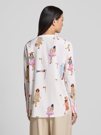 Modelka nosi Relaxed Fit Tunika-Bluse mit Allover-Motiv-Print von HERZENS w jasnych kolorach, wzór z motywem na całej powierzchni, długie rękawy, dekolt z lamówką, długość tyłu 70 cm w rozmiarze 36, długość rękawów 63 cm w rozmiarze 36, tekstura gładka, widok całej sylwetki z tyłu.
