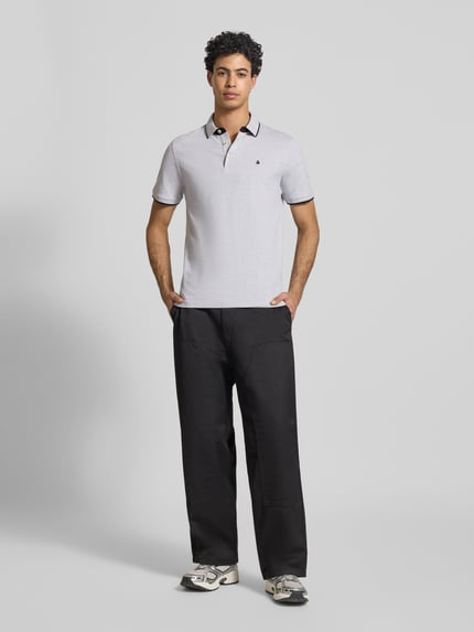 Męski model nosi Koszulkę polo o kroju slim fit z dodatkiem wiskozy Model 'Paulos' od JACK & JONES, mieszanka bawełny i wiskozy, kołnierzyk polo, krótki rękaw, wyhaftowane logo, długość tyłu w rozmiarze M: 72 cm, widok całej sylwetki z przodu.