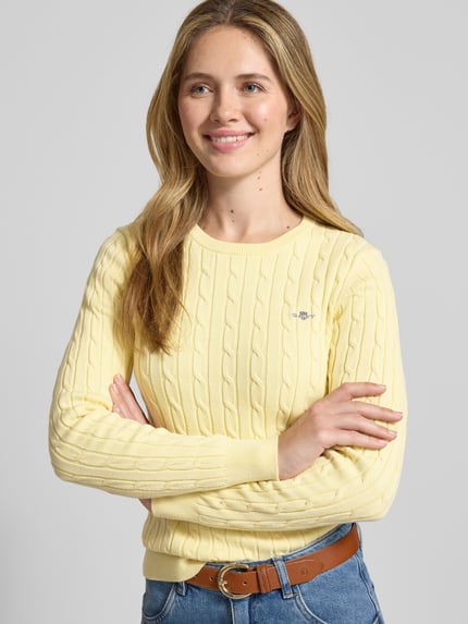 Vrouwenmodel draagt Gebreide pullover met kabelpatroon en labelstitching van Gant, damesmodel, katoenmix met stretch, slim fit, ronde hals, ruglengte maat S 58 cm, mouwlengte 61 cm, geheel vooraanzicht bovenlichaam.
