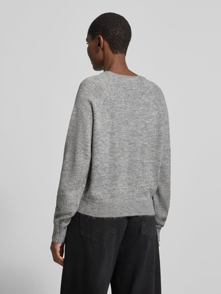 Frauenmodel trägt Pullover mit V-Ausschnitt VMTEAK von VERO MODA in grauer Melange-Strickoptik, Ganzkörperansicht Rückansicht.