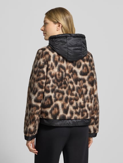 Frauenmodel trägt Mantel mit Kapuze von GIL BRET, Allover-Animal-Print, glänzende Oberfläche, metallische Akzente, Ganzkörperansicht Rückansicht.