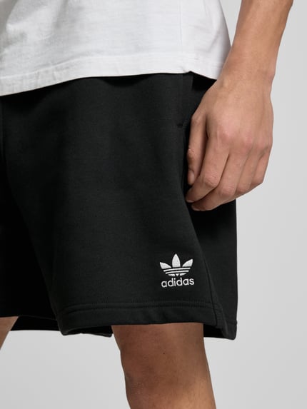 Männermodel trägt Regular Fit Sweatshorts aus katoenmix model 'TREFOIL ESSENTIALS' van adidas Originals, look: effen kleuren, pasvorm: regular fit, applicatie: gestikt logo, boord: elastisch, zakken (onderstuk): zij-steekzakken, materiaalverwerking: sweat, materiaal: katoenmix. Detailaufnahme rechterbeen.