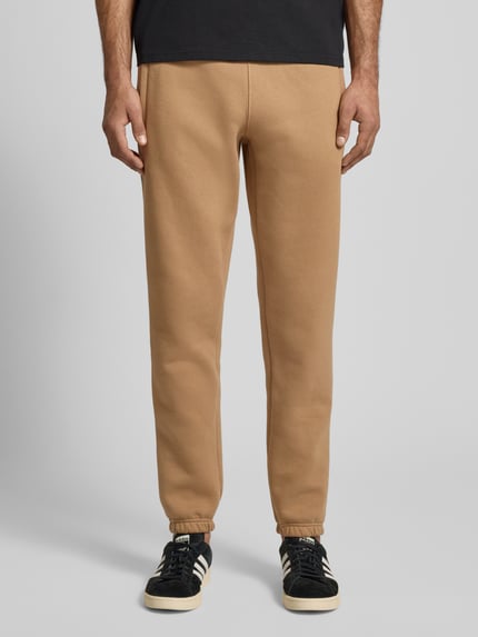 Męski model nosi Sweatpants mit elastischem Bund od adidas Originals, kolor beżowy, luźny krój, widok na całą sylwetkę z przodu.