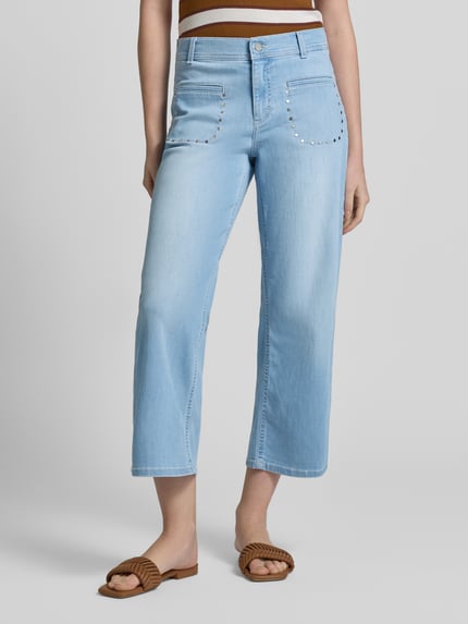 Frauenmodel trägt Wide Fit Jeans in verkürzter Passform Modell 'Linn' von Angels, hellblauer elastischer Baumwoll-Mix mit Nietenbesatz und aufgesetzten Taschen, Ganzkörperansicht von vorne.