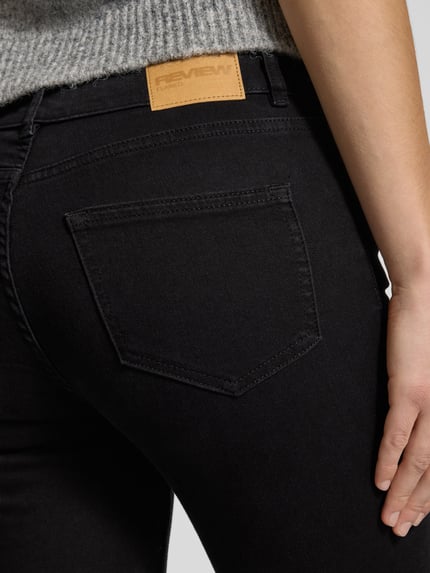 Frauenmodel trägt Flared Jeans mit mittelhohem Bund von Review in schwarzer Waschung, Baumwoll-Mix mit Stretch, Detailaufnahme Rückansicht.