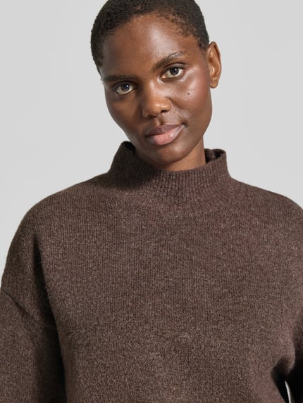 Frauenmodel trägt Turtleneck-Pullover mit Woll-Anteil und Rundhalsausschnitt von Neo Noir in Braun, grobe Struktur, Nahaufnahme Oberkörper.