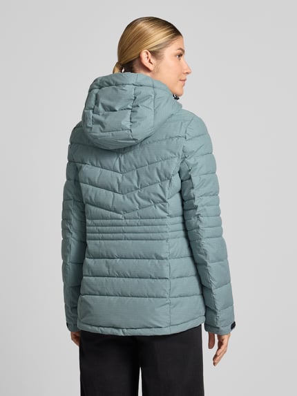 Frauenmodel trägt Jacke mit Kapuze und Label-Patch Modell von G.I.G.A. DX in Hellblau, wattierte Struktur, Ganzkörperansicht Rückansicht. Modell 'KOW10', Kapuze mit Tunnelzug, seitliche Reißverschlusstaschen, Ärmelriegel mit Klettverschluss, 10.000 mm Wassersäule.