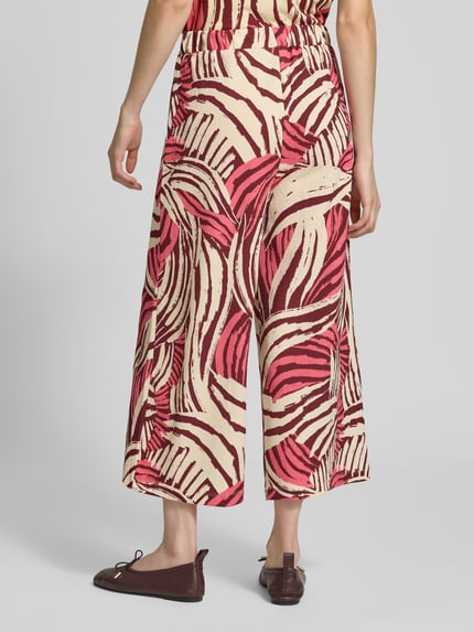 Vrouwenmodel draagt Relaxed Fit Culotte in gestructureerde look van s.Oliver RED LABEL in effen kleuren met elastische boord, steekzakken en jersey materiaalverwerking, high waist pasvorm, structuur en rode/beige tinten, geheellichaamsaanzicht achteraan.