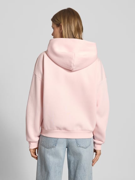Frauenmodel trägt Sweatjacke mit Logo und Känguru-Tasche von Review in Rosa, Baumwoll-Mix, Relaxed Fit, Ganzkörperansicht Rückansicht.
