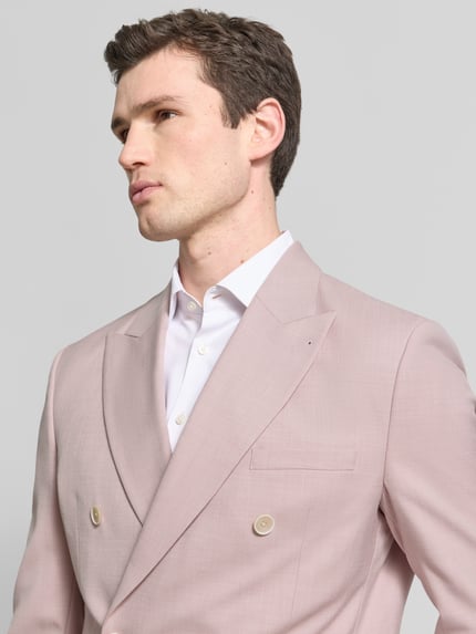 Męski model nosi Slim Fit Anzugjacke mit Reverskragen von MCNEAL, kolor jasnoróżowy, z podwójnym zapięciem, krój slim fit, detaliczna kieszeń na piersi, widoczna faktura materiału, zbliżenie na górną część ciała, nahaufnahme oberkörper. Długość tyłu w rozmiarze 52: 75 cm, szerokość ramion w rozmiarze 52: 45 cm, długość rękawa w rozmiarze 52: 66 cm.