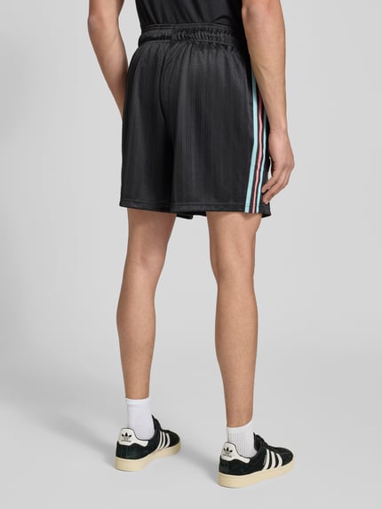 Männermodel trägt Regular Fit Sweatpants mit Label-Detail Modell 'Belgien 26' van adidas Originals in effen zwart met elastische tailleband en zijzakken, sweatmateriaal, ganzkörperansicht rückansicht.