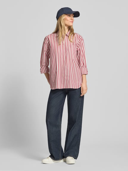 Frauenmodel trägt Regular Fit Langarmbluse aus reiner Baumwolle von Tommy Hilfiger, Optik:Allover-Muster, Streifen-Optik, Popeline, Logo-Stitching, Hemdkragen, einreihige Knopfleiste, Brusttasche, Langarm, Manschette, abgerundeter Rumpfabschluss, Regular-Fit, Unifarben und gestreift, Ganzkörperansicht von vorne.