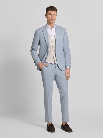 Männermodel trägt Weste mit V-Ausschnitt und Leistentaschen von Wilvorst in Beige, gerader Schnitt, kombiniert mit hellblauem Anzug, Ganzkörperansicht von vorne.