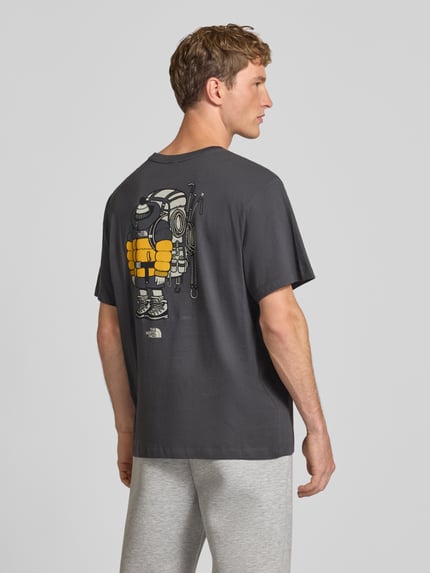 Männermodel trägt T-Shirt aus reiner Baumwolle Modell 'Gear Up Get Out' von The North Face in Dunkelgrau mit Logo-Print, Ganzkörperansicht Rückansicht.