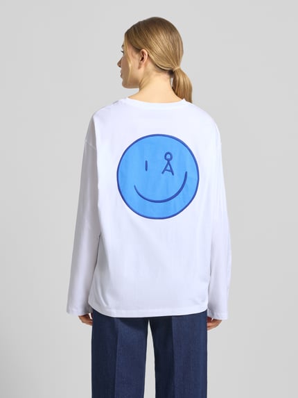 Vrouwenmodel draagt oversized langarmshirt uit pure katoen, model 'FIETAA SMILE' van Armedangels, wit met blauwe smiley, unicolor, logo-stitching, labeltekst, fijne ribstructuur, dames, volledig van achteren.