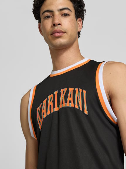 Männermodel trägt Regular Fit Top mit Logo-Print von KARL KANI in Schwarz mit Strukturmuster und Rundhalsausschnitt, Nahaufnahme Oberkörper. Rückenlänge bei Größe M: 75 cm.