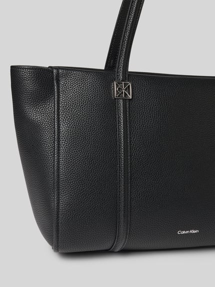 Produktfoto, Shopper met Labeldetail van CK Calvin Klein, zwart, structuurleer, metalen label, draagband, hoofdvak met ritssluiting, binnenvak met rits, breedte 47 cm, lengte 26 cm, diepte 16 cm, schouderband 63 cm.