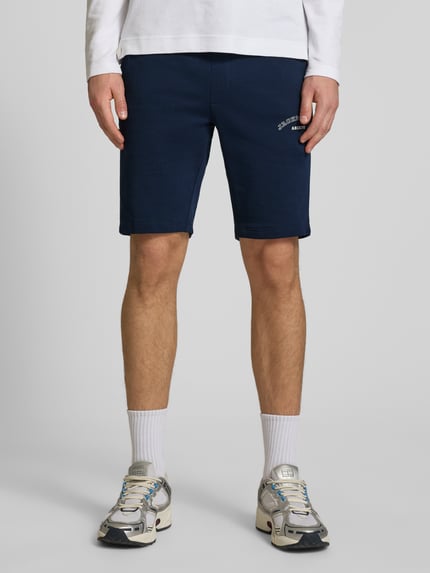 Männermodel trägt dunkelblaue Shorts mit Logo-Print Modell 'GORDON' von Jack & Jones aus Baumwoll-Mix, Relaxed Fit, Ganzkörperansicht von vorne.