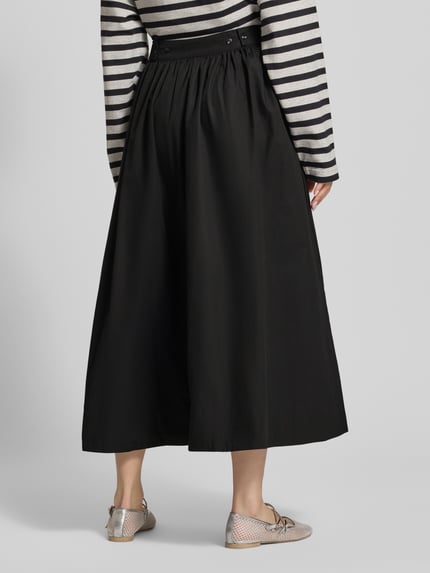 Frauenmodel trägt schwarzen Midirock mit A-Linie aus reiner Baumwolle, Modell 'SALLY' von Topshop, seitlicher Reißverschluss, Ganzkörperansicht Rückansicht. Bundweite bei Größe 36: 35 cm.