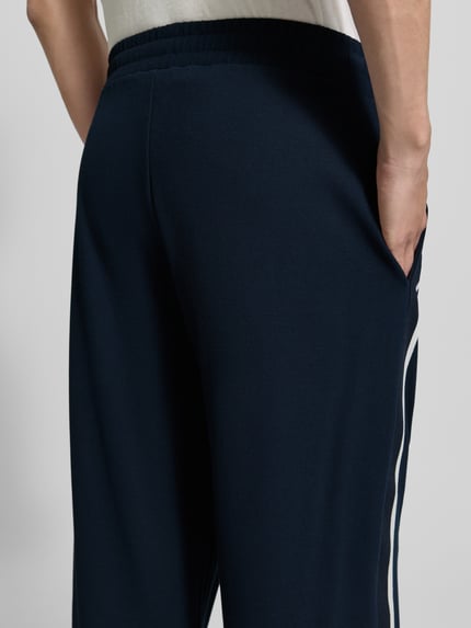 Mężczyznamodel nosi spodnie typu track pants z mieszanki wiskozy EA7 Emporio Armani, ozdobne szwy, wpuszczane kieszenie, lampasy, detailaufnahme.