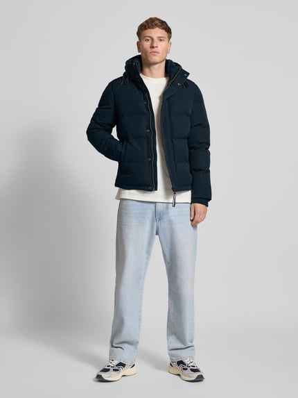Männermodel trägt dunkelblaue Steppjacke mit Eingrifftaschen Modell 'Everest' von Superdry, Regular-Fit, Kapuze, Label-Detail, Ganzkörperansicht von vorne, Rückenlänge bei Größe M 66 cm, Schulterbreite 48 cm, Brustweite 42 cm, Ärmellänge 70 cm.