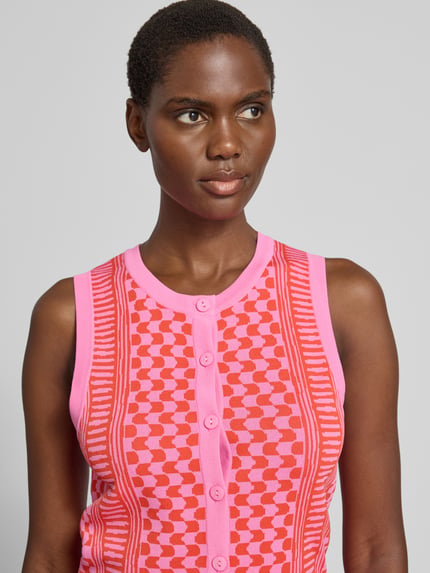 Kobiece modelka nosi Strickweste aus Viskose-Mix Modell 'GABLESI' od SUNCOO PARIS, wzór geometryczny, różowe i czerwone kolory, dopasowany krój slim fit, okrągły dekolt, bez rękawów, ozdobna listwa guzikowa, długość pleców w rozmiarze S: 47 cm, zbliżenie na górną część ciała.