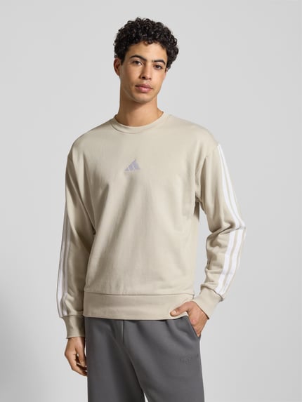 Männermodel trägt Sweatshirt mit Label-Stitching von adidas Sportswear, Baumwoll-Mix mit Viskose-Anteil, lockerer Schnitt, Rundhalsausschnitt, gerippte Abschlüsse, Rückenlänge 68 cm, Ärmellänge 62 cm, helle Farben, weiche Textur, Ganzkörperansicht von vorne.