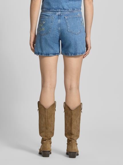 Frauenmodel trägt Regular Fit Jeansshorts aus reiner Baumwolle Modell 'SKY' von Pieces in Denim-Optik mit Stickerei, Nieten, 5-Pocket-Design, Ganzkörperansicht Rückansicht.