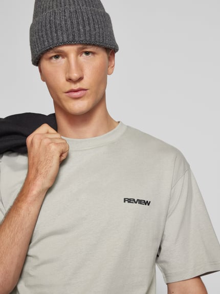 Männermodel trägt Relaxed Fit T-Shirt aus reiner Baumwolle von REVIEW in hellem Grau, Logo-Stickerei, Nahaufnahme Oberkörper.