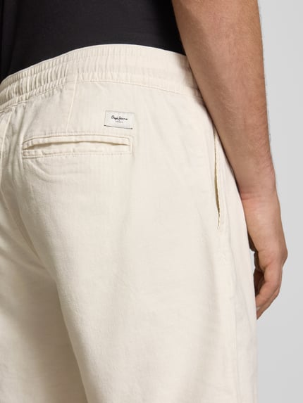 Mężczyzna nosi Relaxed Fit Chinoshorts aus Baumwoll-Leinen-Mix od Pepe Jeans, jasny kolor, tekstura gładka, detal tylnej kieszeni, zbliżenie na biodra.