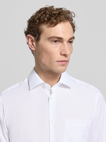 Männermodel trägt Regular Fit Business-Hemd mit Kentkragen von SEIDENSTICKER, reine Baumwolle, weiß, sichtbare Brusttasche, Knopfleiste, Nahaufnahme Oberkörper.