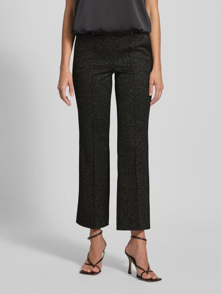 Vrouwenmodel draagt Stoffhose in verkürzter Passform Modell 'FRANCOISE' van Cambio, zwarte glinsterstof, rechte snit, verkorte lengte, glittereffect, elastische tailleband, Franse steekzakken, achterzakken, mix van viscose. Ganzkörperansicht van voren.