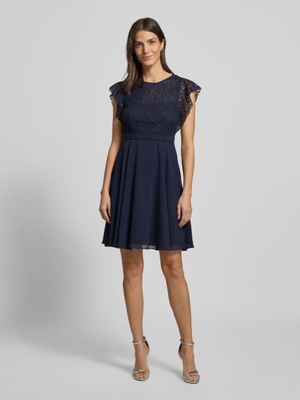 Frauenmodel trägt Knielanges Cocktailkleid mit Rundhalsausschnitt von Jake*s Cocktail, taillierter Schnitt, blickdichtes Unterkleid, Nahtreißverschluss, dunkelblau, Ganzkörperansicht von vorne. Rückenlänge bei Größe 36: 90 cm, Brustweite 35 cm, Ärmellänge 10 cm.