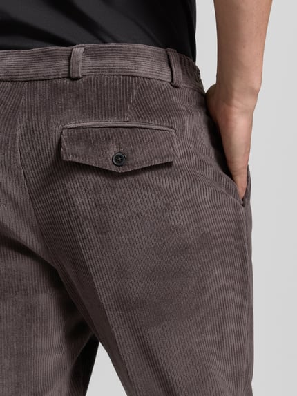 Männermodel trägt Slim Fit Hose aus Baumwoll-Mix in Cord-Optik Modell 'Cliffer' von Zuitable, brauner Stoff, Detailaufnahme Rückansicht, elastischer Bund, Eingriff- und Gesäßtaschen, Knopf- und Reißverschluss, neutrale Beleuchtung, Kontext: Bundweite 37 cm, Innenbeinlänge 76 cm, KI-modifiziertes Bild.