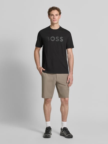 Męski model nosi Regular Fit T-Shirt aus reiner Baumwolle Modell 'TS_STRUCTURE LOGO 1027473' von BOSS Green, czarna koszulka z nadrukiem, krój regular fit, gładka tekstura, Ganzkörperansicht von vorne.