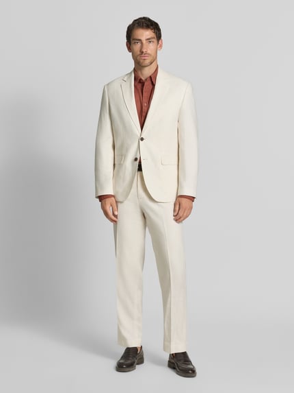 Männermodel trägt Regular Fit Sakko aus Leinen-Baumwoll-Mix von Selected in Creme mit braunem Hemd und Anzughose, Ganzkörperansicht von vorne.
