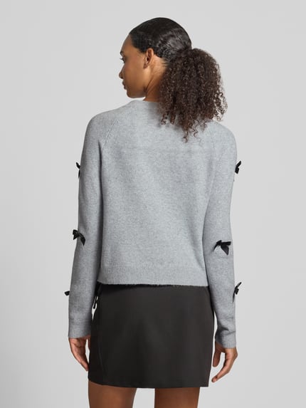 Frauenmodel trägt Regular Fit Pullover mit Raglanärmeln Modell 'NOELLE' von ONLY in Hellgrau mit schwarzen Schleifen, Ganzkörperansicht Rückansicht. Damen Pullover von ONLY
