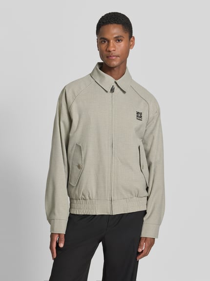 Męskimodel nosi Regular Fit Blouson mit Logo-Detail Modell 'Bartos' von HUGO, efekt: wzór na całej powierzchni, aplikacja z logo, krój regular fit, zamek błyskawiczny, ściągacz, wpuszczane kieszenie z guzikami, jasny beż z mikrowzorem, tkanina lekko fakturowana. Ganzkörperansicht z przodu.