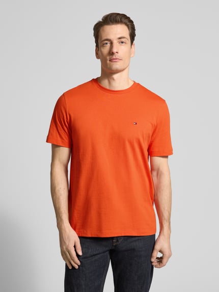 Männermodel trägt Regular Fit T-Shirt aus reiner Baumwolle von Tommy Hilfiger in Unifarbe Orange, Logo-Stitching, Ganzkörperansicht von vorne.