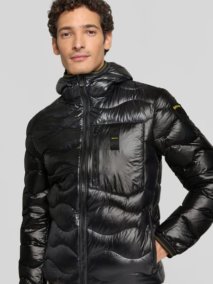 Männermodel trägt Steppjacke mit Zweiwege-Reißverschluss Modell 'WAVE' von Blauer USA in Schwarz, glänzende Oberfläche, Nahaufnahme Oberkörper. Rückenlänge Größe M 68 cm, Schulterbreite 47 cm, Brustweite 53 cm, Ärmellänge 49 cm, Slim Fit, Kapuze, Label-Detail.