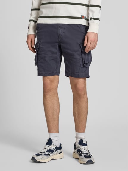 Männermodel trägt Straight Fit Shorts mit Cargo-Taschen Modell 'Core' von Superdry aus Baumwoll-Mix, dunkelblau, Ganzkörperansicht von vorne. Bundweite 42 cm, Innenbeinlänge 23 cm, mit Knopf- und Reißverschluss, Eingriff- und Gesäßtaschen.