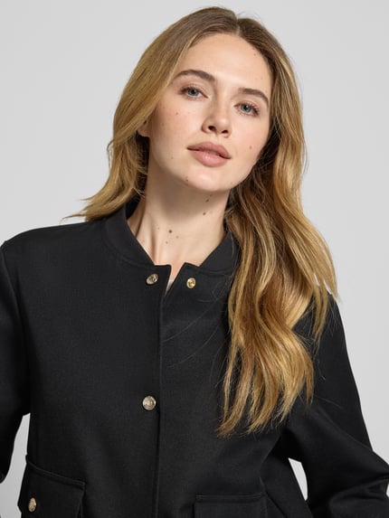 Frauenmodel trägt schwarze Jacke mit Stehkragen Modell 'Orlanda' von JOOP!, Regular-Fit, Knopfleiste, Pattentaschen, Nahaufnahme Oberkörper. Rückenlänge 53 cm, Schulterbreite 44 cm, Brustweite 53 cm, Ärmellänge 59 cm bei Größe 36.