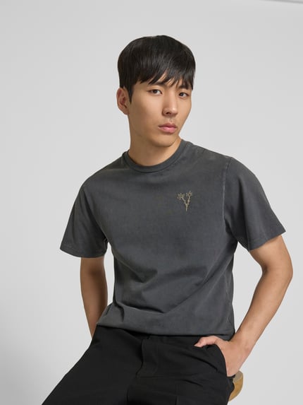 Männermodel trägt T-Shirt mit floralem Stitching von Forét in Dunkelgrau, Reine Baumwolle, Regular-Fit, Rundhalsausschnitt, Kurzärmelig, Ganzkörperansicht von vorne.
