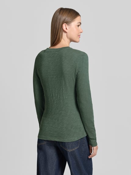 Vrouwenmodel draagt Langarmshirt mit abgerundetem Saum van MARC O'POLO in effen groen, ronde hals, lange mouw, afgeronde zoom, volledige lichaamsaanzicht achteraan.