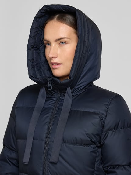 Frauenmodel trägt Regular Fit Daunenmantel mit Label-Print von Marc O'Polo in Dunkelblau mit glatter, gesteppter Oberfläche, Nahaufnahme Oberkörper. Damen Daunenmantel von Marc O'Polo.