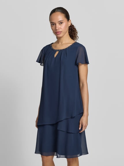 Frauenmodel trägt knielanges Cocktailkleid mit Schlüsselloch-Ausschnitt von Christian Berg Cocktail aus Chiffon im Stufen-Look mit Perlen, Gerader-Schnitt, dunkelblau, Ganzkörperansicht von vorne. Rückenlänge bei Größe 36: 93 cm, Brustweite: 47 cm, Ärmellänge: 12 cm.