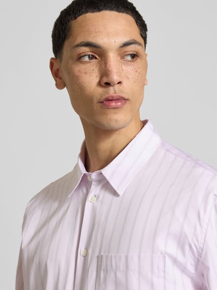 Männermodel trägt Relaxed Fit Freizeithemd aus bawełna von MAISON KITSUNÉ, jasne kolory, na całej długości listwa guzikowa, brustasza, krój z długim rękawem, długość tyłu w rozmiarze M: 74 cm, szerokość w rozmiarze M: 49 cm, długość rękawów w rozmiarze M: 68 cm, zbliżenie na górną część ciała